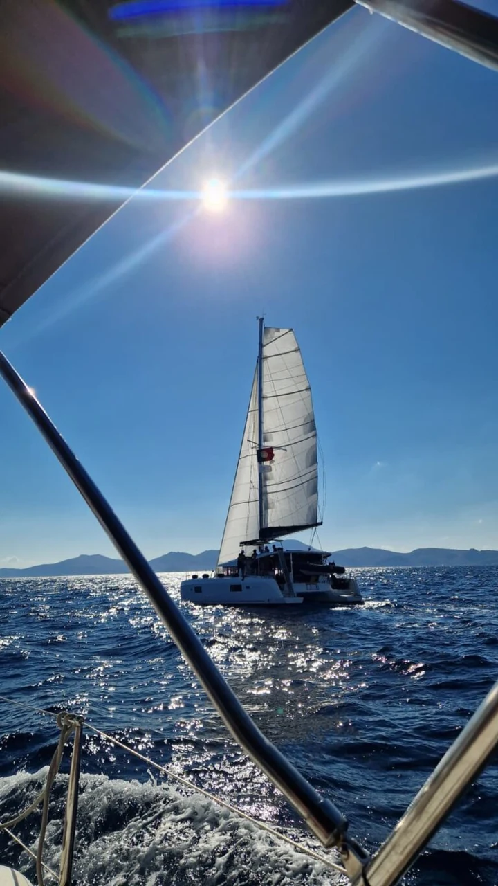 Catamarã à vela e água junto à embarcação ao sol.