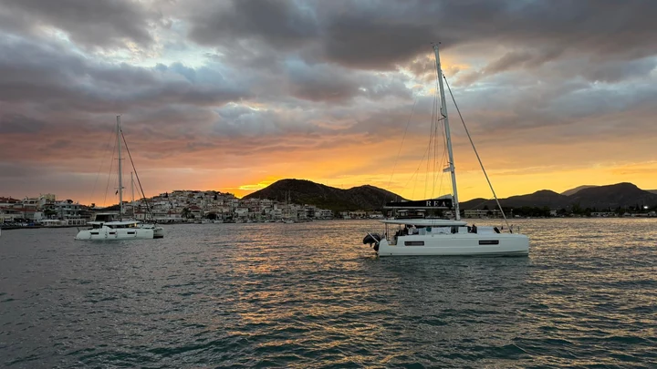 Catamarãs fundeados diante de uma povoação ao pôr do sol.